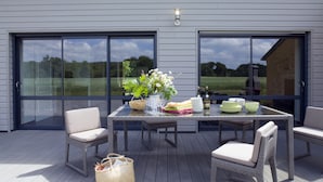 Un patio al aire libre con una mesa lista para comer, sillas de mimbre, una cesta tejida y un florero con flores.