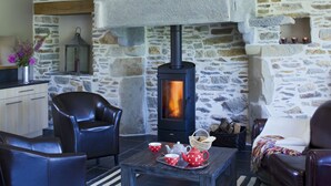 Un cuarto acogedor con pared de piedra, chimenea, sillones de cuero, una mesa con una bandeja de té y una tetera, y una cesta de pan.