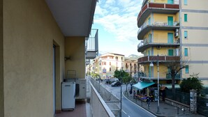 A balcony with a view of a street, a vending machine, and a small outdoor market. - Apartment Giusy - central (SORRENTO)