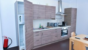 A compact kitchen with a stove, microwave, and sink, wooden cabinets, and a fire extinguisher. - Apartment Giusy - central (SORRENTO)