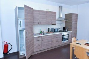 A compact kitchen with a stove, microwave, and sink, wooden cabinets, and a fire extinguisher.