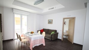 A dining area with a table set for four, a sofa, and a door leading to another room. - Apartment Giusy - central (SORRENTO)