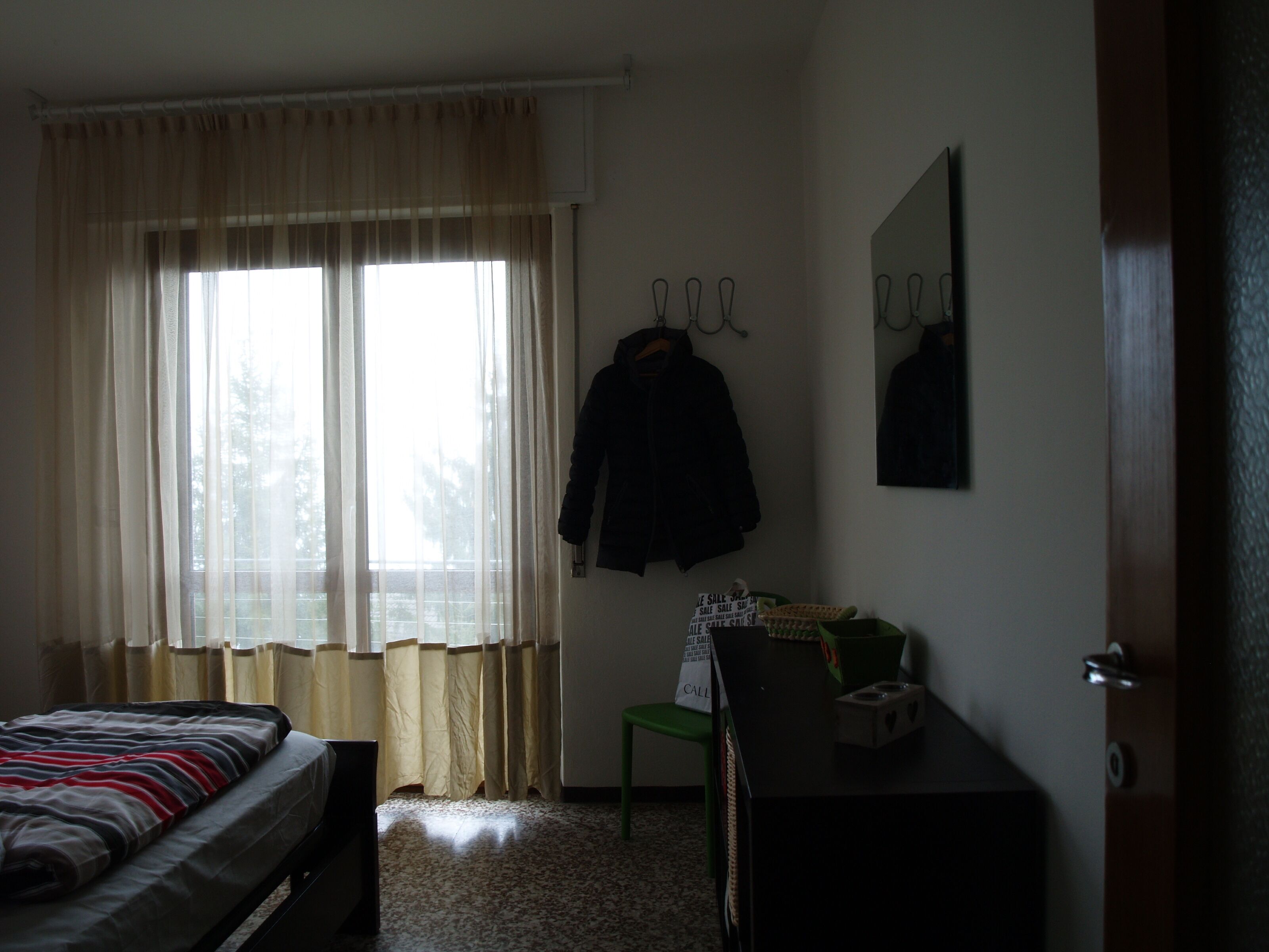 Une chambre à coucher comprenant un lit, un bureau, une chaise, un porte-manteau et une fenêtre avec des rideaux.