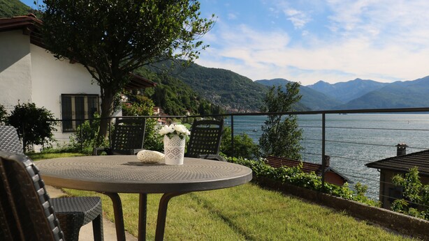 Une table ronde entourée de chaises, avec un vase de fleurs, donnant sur un lac bordé de montagnes.
