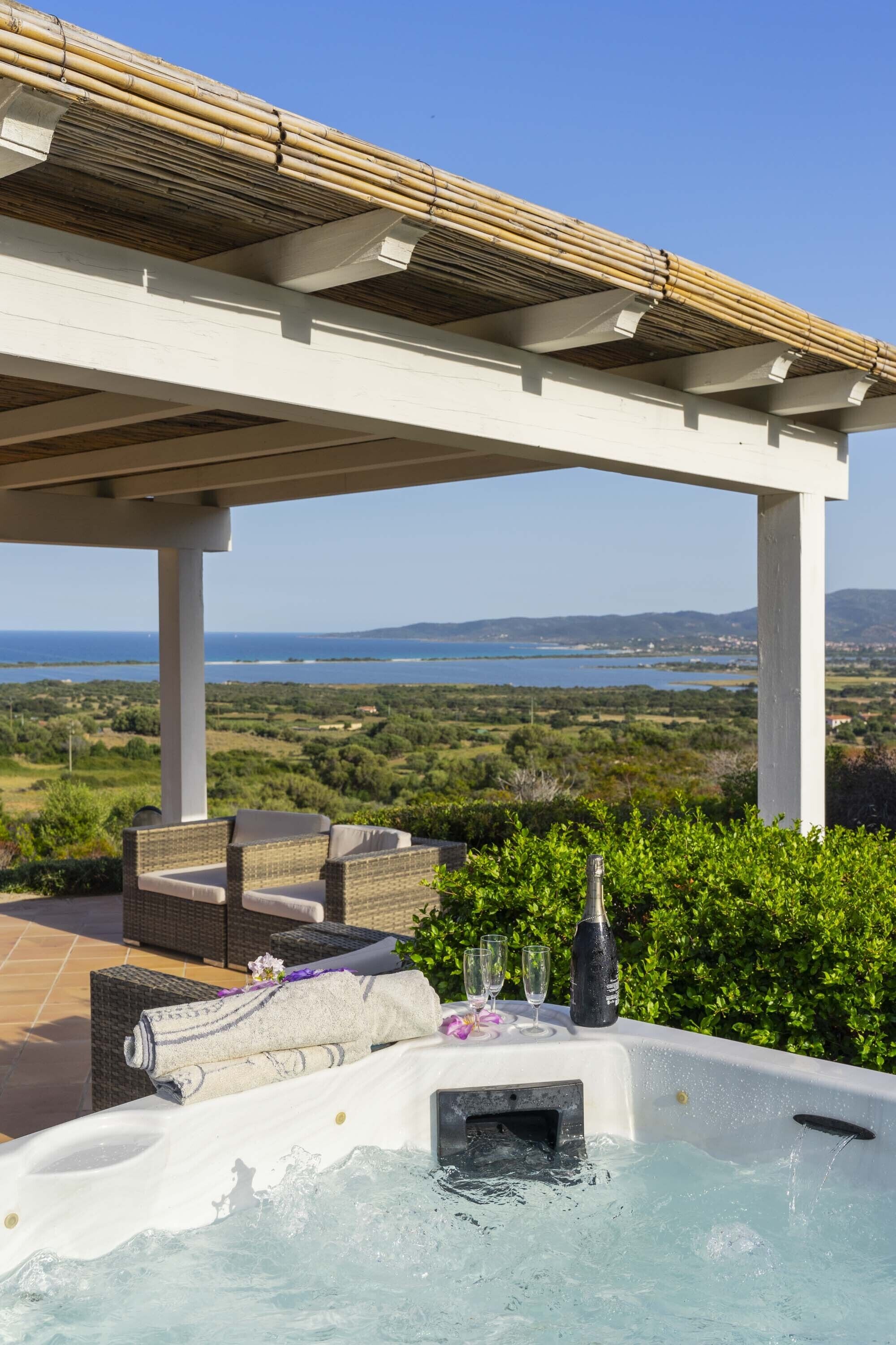 A hot tub with a view of the sea, outdoor seating, and a pergola structure.