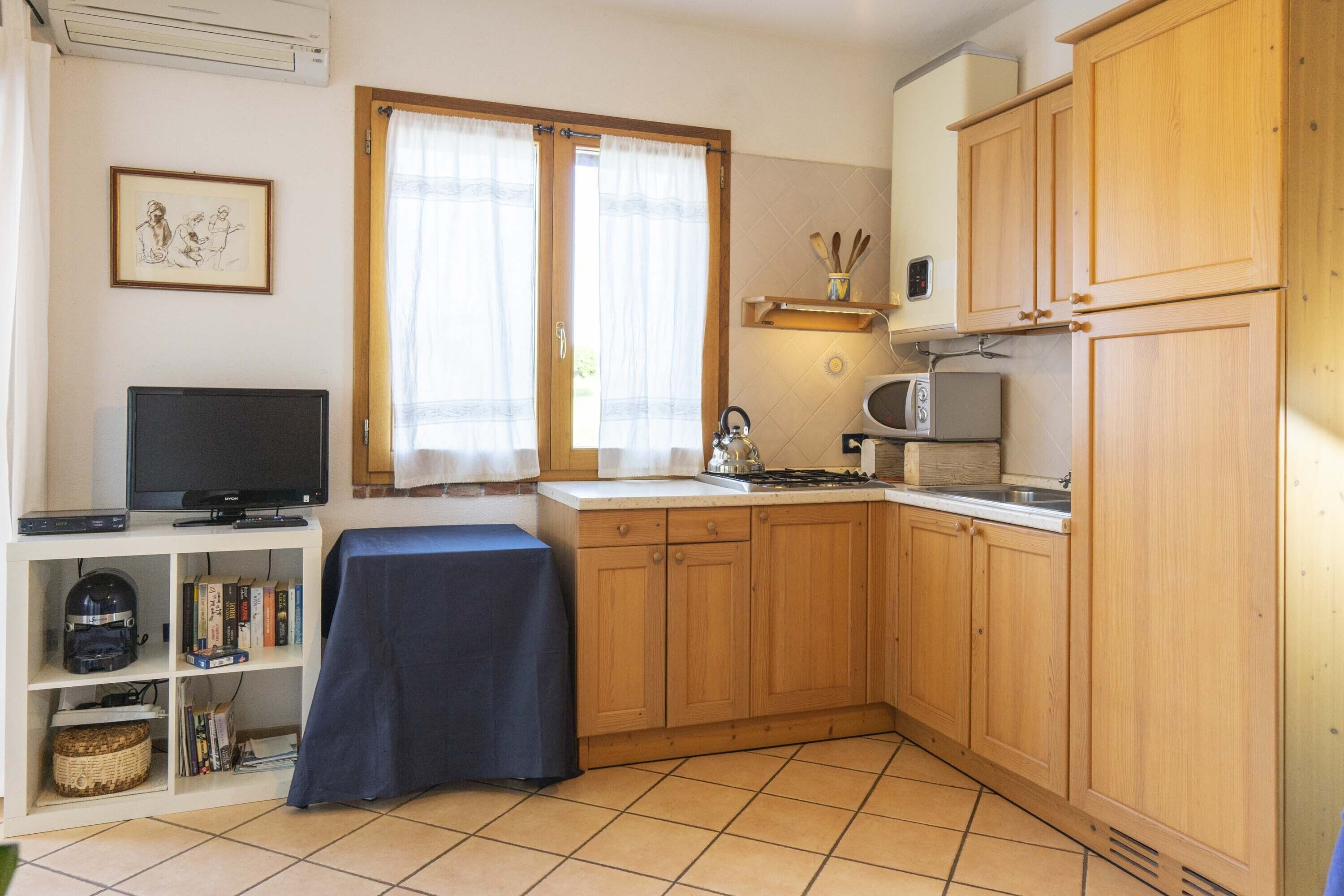 Une cuisine compacte avec des meubles de rangement en bois, un four à micro-ondes, un évier et un téléviseur posé sur une étagère.