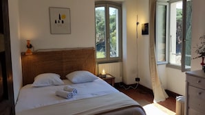A bedroom with a large bed, a bedside table, a nightstand, a floor lamp, a dresser, and a window with a view of greenery. - Mansion - Port -vendres (Port-Vendres)