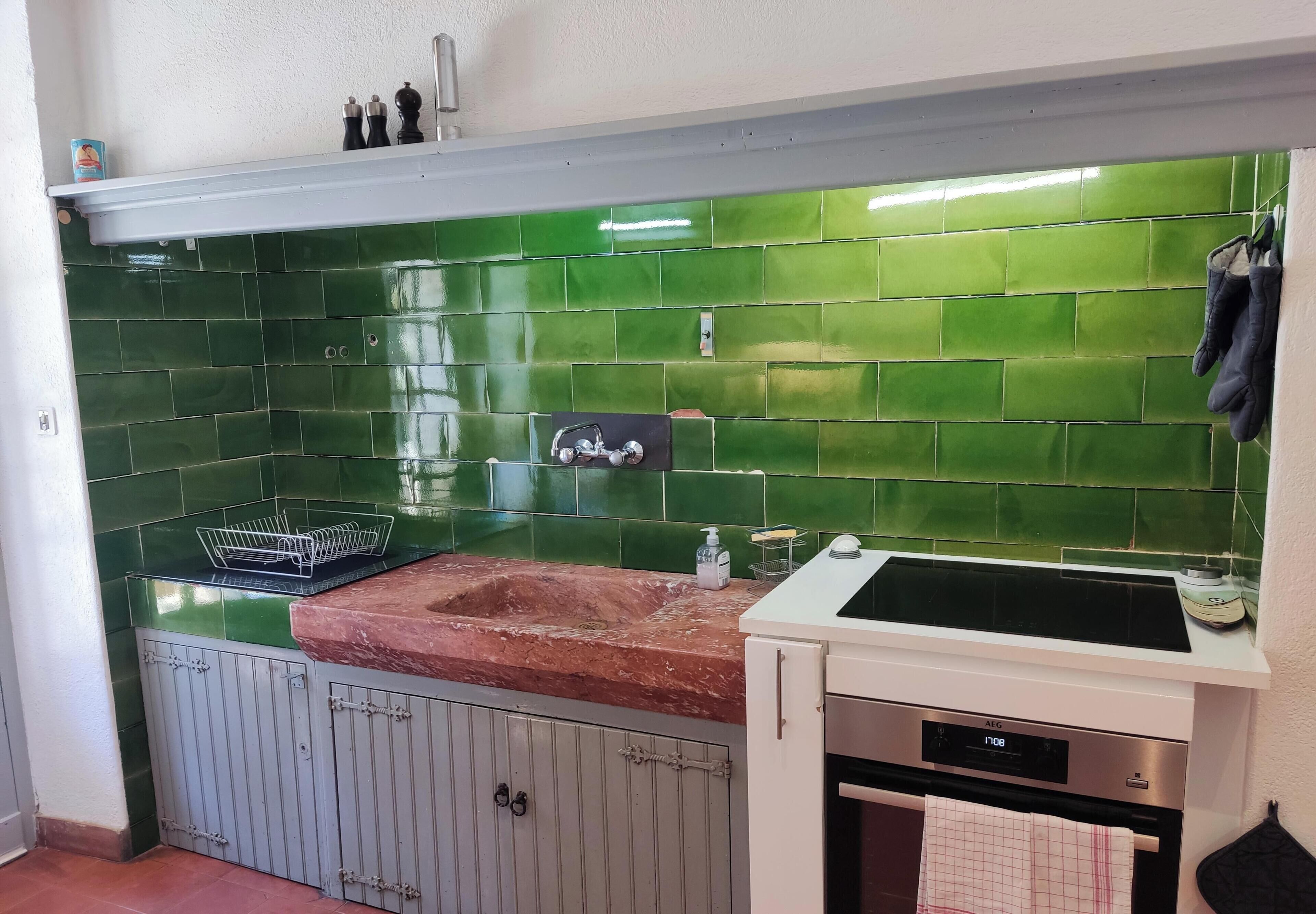 Une cuisine avec des carreaux verts, un évier, une cuisinière et un placard.