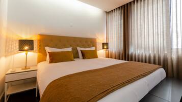 A hotel room with a large bed, two bedside lamps, a nightstand, and a window with curtains.