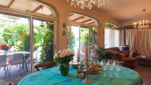A dining area with a table set for a meal, a chandelier, and a view of the garden through glass doors. - La Bouganville swimming pool & relaxation (Camaiore)
