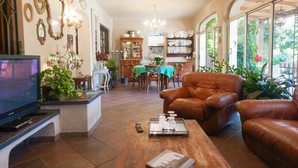 A spacious living room with a television, leather sofas, a wooden coffee table, and a dining area with a green tablecloth. - La Bouganville swimming pool & relaxation (Camaiore)