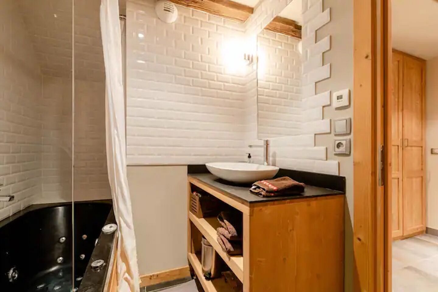 Een moderne badkamer met een glazen douchecabine, een witte baksteenmuur, een houten wastafelmeubel en een zwart bad.