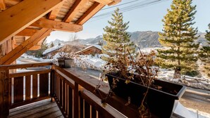 Un balcon en bois offrant une vue sur des montagnes enneigées et des pins.