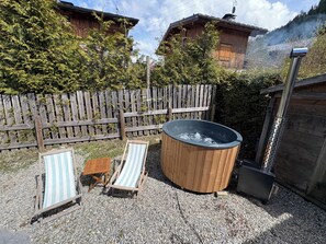 A wooden hot tub with two striped lounge chairs, surrounded by a wooden fence and gravel ground, with a mountain backdrop. - Megeve-Rochebrune Chalet(Ski Direct In and OUT) with outdoor jacuzzieur 10 pers (Megève)