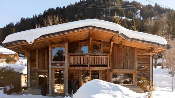 Une cabane en bois dotée d’un balcon, entourée de neige et de montagnes boisées.
