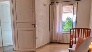 Una habitación con una cama, una silla, un ventanal con cortinas y un radiador.