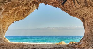 A cave opening to a beach with clear blue water and distant rocky formations. - GRREN HOUSE 
APPARTMENT WITH GARDEN,  veranda and barbecue, 1,5KM BY SEA (Siniscola)