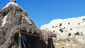 Una cabaña de piedra con techo de paja, con montañas al fondo.