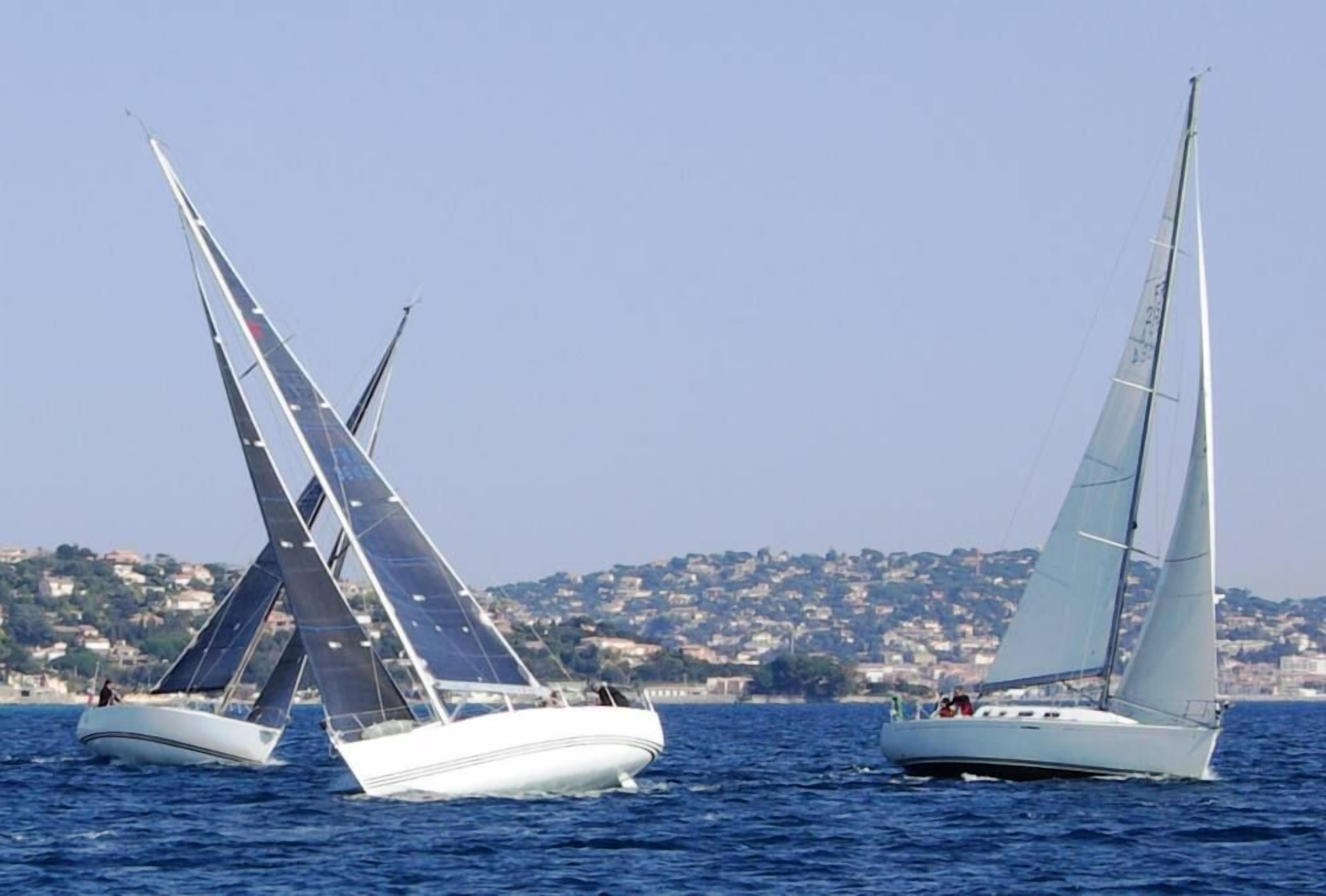 Two sailboats on a calm sea with a coastal town in the background.