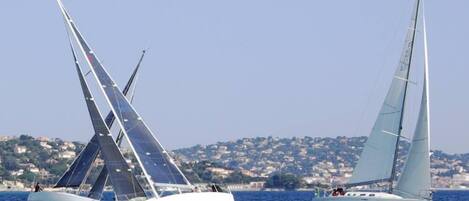 Two sailboats on a calm sea with a coastal town in the background.