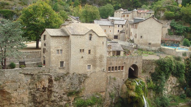 Un edificio in pietra con una cascata, una piscina e un ponte.