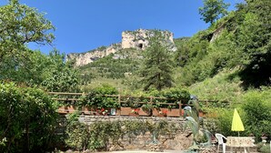 Area piscina con pavimento in legno, muro in pietra e vista su una montagna con una struttura simile a una grotta.