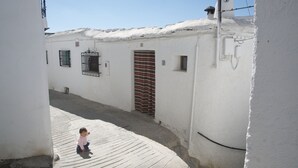 Une ruelle étroite bordée de bâtiments blancs, avec une porte à rayures et une petite fenêtre.