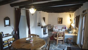 Un salon chaleureux avec un sol en pierre, des meubles en bois, une cheminée et un coin repas comprenant une table ronde et des chaises.
