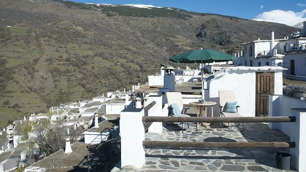 Un bâtiment blanc doté d’une terrasse en pierre, d’un parasol vert et offrant une vue sur un paysage montagneux.