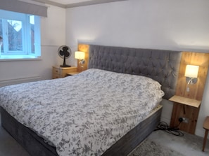 Une chambre avec un grand lit, une table de chevet, un ventilateur fixé au mur et deux lampes de chevet.