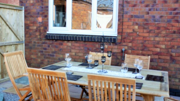 A wooden table set for four with wine glasses and a menu, against a brick wall with a window.