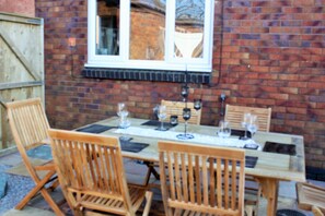 Une table en bois, dressée pour quatre personnes, avec des verres à vin et un menu, placée devant un mur de briques avec une fenêtre.