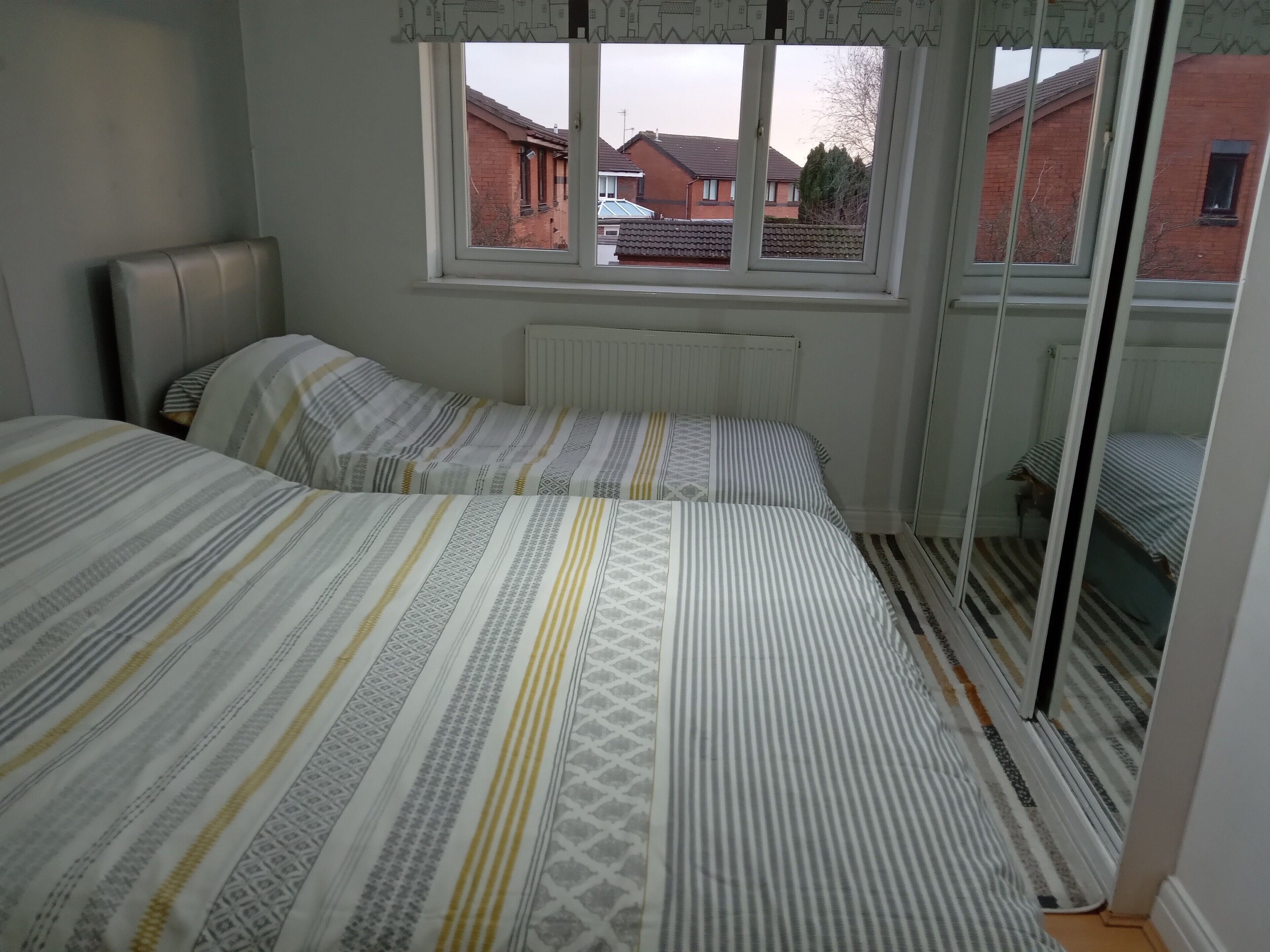Un dormitorio con dos camas, una ventana con vista a casas y un radiador.
