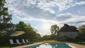 A swimming pool with lounge chairs and an umbrella, surrounded by greenery and a stone building. - Elegant 7-Bedroom Château in Burgundy Wine Country Near Chablis & Auxerre (Hauterive)