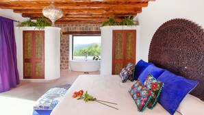 Une chambre avec un grand lit, une vue sur l’extérieur, un plafond en bois et une tête de lit décorative.