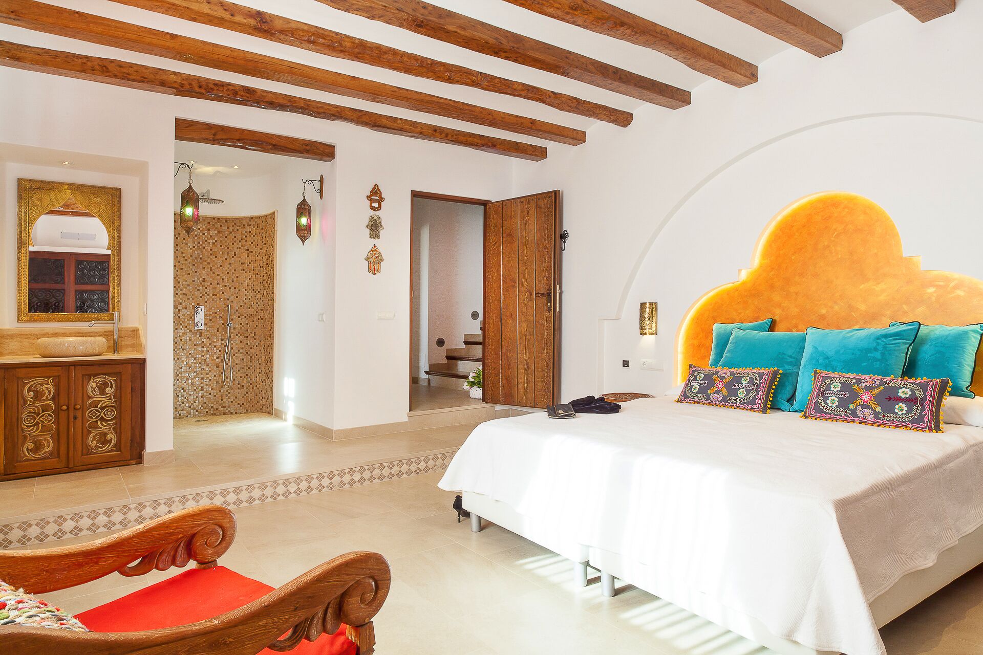 A bedroom with a large bed, a wooden headboard, a wooden wardrobe, and a bathroom with a mosaic wall.