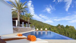 Un espace aménagé au bord de la piscine, avec des chaises longues et un mur en pierre, offrant une vue sur une colline.