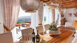 Un coin repas avec une table en bois, des chaises, un plateau avec des verres et une bouteille, et des lampes suspendues.