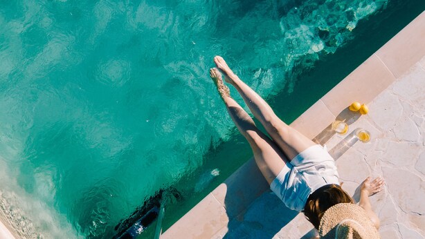 Eine Person entspannt am Pool mit klarem Wasser, einer Steindeck und einer Liege.