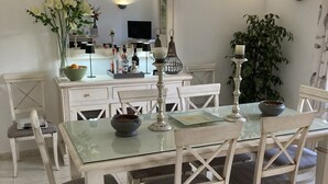 Un coin repas avec une table en verre, des chaises blanches, un miroir et une plante en pot.
