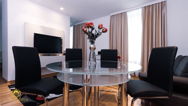 Ein modernes Wohnzimmer mit Glastisch, schwarzen Stühlen, einem Flachbildfernseher und einer Vase mit Blumen.