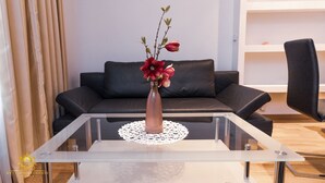 Ein modernes Wohnzimmer mit einem Glastisch, einer Blumenvase, einem schwarzen Ledersofa und einem weißen Regal.