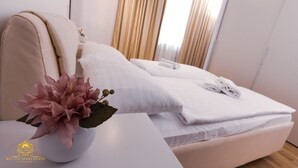 Ein Hotelzimmer mit Bett, Kissen, einer Vase mit Blumen und einem ordentlich bezogenen Bett mit Handtüchern.