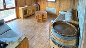 Interior de una cabaña de madera con cocina, un sofá, una mesa de comedor y un barril grande.