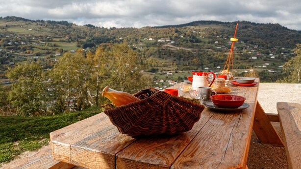 Un juego de mesa de picnic de madera montado al aire libre, con una cesta, platos y una botella.