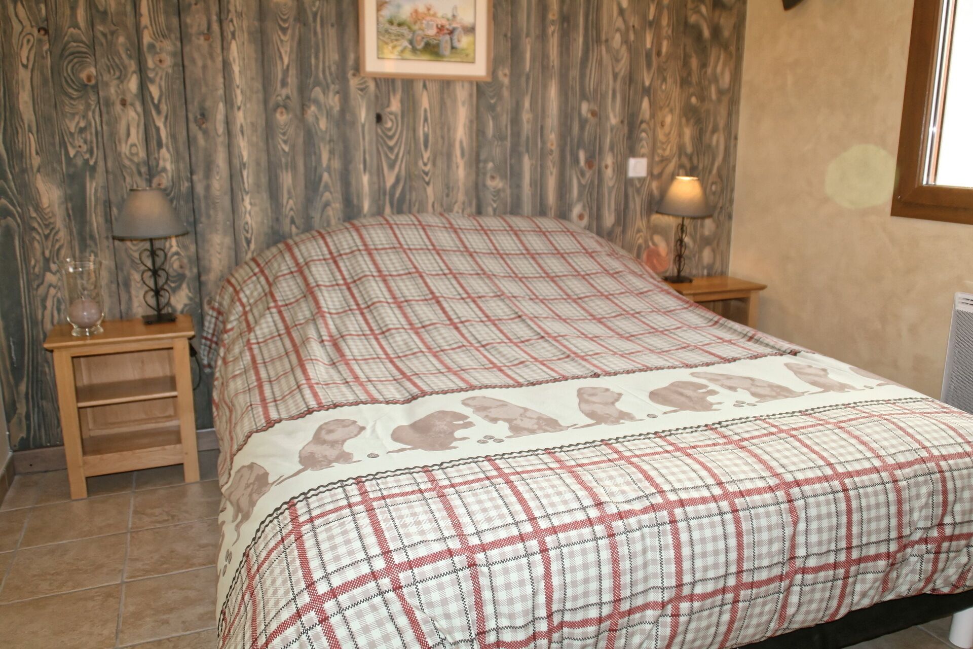 Un dormitorio con colcha escocesa, mesitas de noche de madera, una lámpara y un cuadro en la pared.