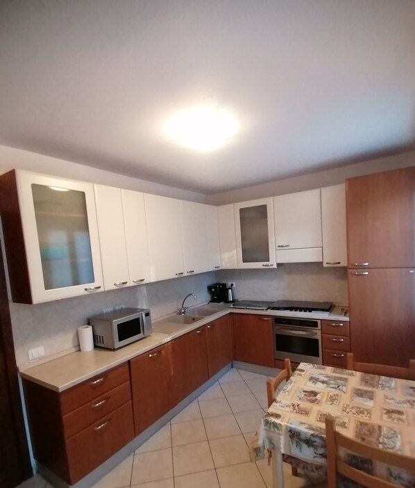 A compact kitchen with white and wooden cabinets, a microwave, a stove, and a sink.