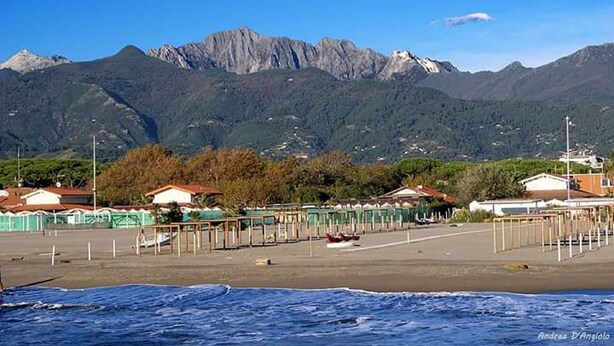 Ein Strand mit Bergblick, einem eingezäunten Bereich und einigen Gebäuden.