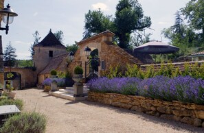 A stone building with a tiled roof, a small archway, and a gravel pathway leading to it.