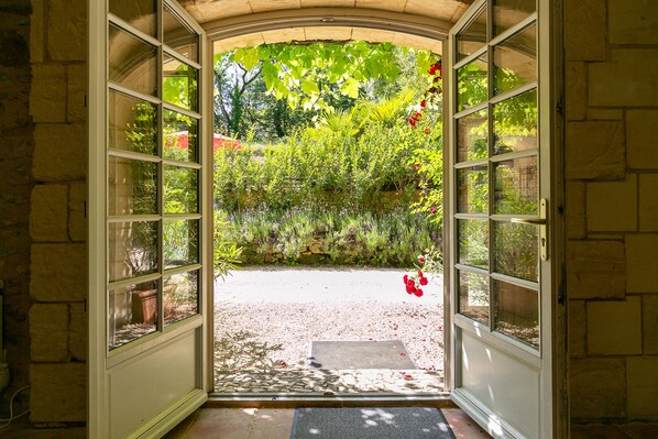 An open doorway leading to a garden with a gravel path and a small entrance mat.